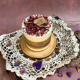 Handcrafted medium candle topped with rose petals on crystal pedestal surrounded by eucalyptus and scattered rose petals