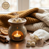 White linen bag filled with handmade orange and cinnamon scented soy wax melts with shredded cinnamon, displayed on a rustic wooden table next to an oil burner, cinnamon sticks, and dried orange slices.