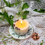 Burning coffee candle on ceramic plate with melting wax pool and coffee beans visible