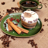 Handmade small coffee scented candle with kraft paper tag on elegant green plate styled with cinnamon sticks, red berries and scattered coffee beans