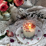 Rose petal scented candle in romantic table setting with vintage china, fresh roses, and scattered rose petals on lace
