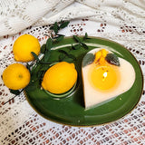 Heart-shaped candle with lemons on a green plate with lemons and leaves on a lace tablecloth.