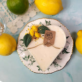 Heart-shaped candle on a decorative plate with lemons and a tag on a light blue background