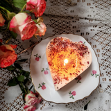 Handcrafted small heart rose petals candle with warm flame styled on vintage floral china with lace and fresh pink roses