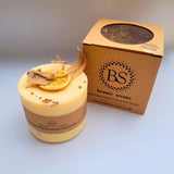 Large handmade scented candle by Beauty Scents, decorated with a dried orange slice and cinnamon stick pieces, shown against a plain light background.