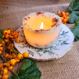 Candle on a decorative plate with berries and leaves on a textured surface