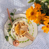 Decorative candle on the  plate with dried orange slices, a wooden tag, and a bouquet of yellow flowers on a textured white background.
