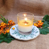 Candle in a glass holder on a decorative plate with berries and leaves on a burlap background