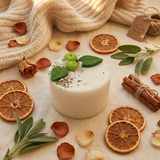 Beauty Scents small apple candle with green leaves on a beige surface with dried oranges and cinnamon sticks. Next to textile material. 