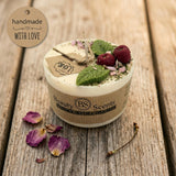 Small soy candle with cherry wax melt decoration and green leaf detail, with a ‘handmade with love’ tag and label, styled on a rustic wooden surface with dried petals.