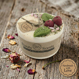 Small soy candle with cherry wax melt decoration and green leaf detail, with a ‘handmade with love’ tag and label, styled on a rustic wooden surface with dried petals. Close up