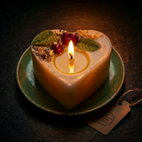 Lit heart-shaped soy candle with a melted wax pool, decorated with cherry wax melts and green leaf details on a green ceramic plate in cosy low night light.