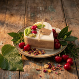 Small heart-shaped soy candle with cherry wax melt decoration and green leaf detail on a plate on a rustic wooden table in warm evening light, styled with fresh cherries and greenery.