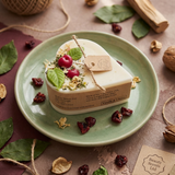 Small heart-shaped soy candle with cherry wax melt decoration and green leaf detail on a green ceramic plate in daylight, styled with dried botanicals.