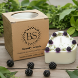 Heart-shaped candle with blackberries and a 'Beauty Scents' box on a wooden surface with greenery.