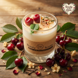 Small soy candle in a glass jar with wax cherries and green leaf decoration on a wooden table, styled with fresh cherries, green leaves and dried flower petals
