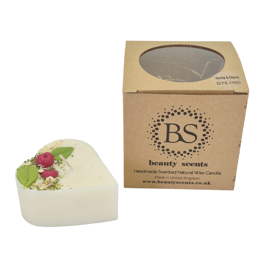 Heart-shaped candle with wax cherries and green leafs on a white background next to a cardboard box labeled 'Beauty Scents'.