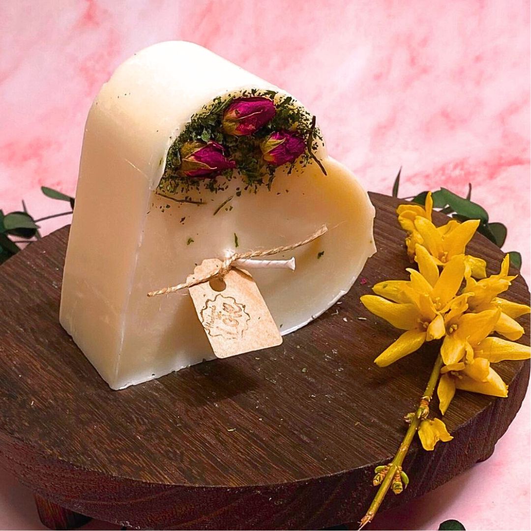 Heart-shaped candle with flowers on a wooden stand against a pink background