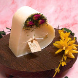 Heart-shaped candle with flowers on a wooden stand against a pink background
