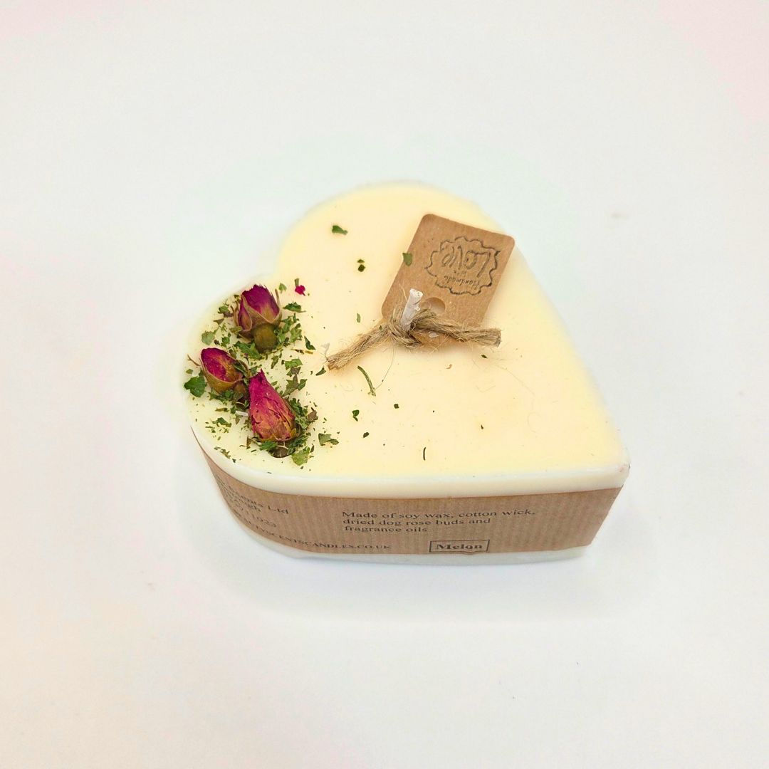 Heart-shaped candle with dried flowers and a brand tag on a light gray background