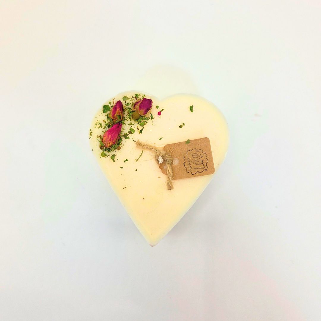 Heart-shaped candle with dried flowers and a tag on a light background