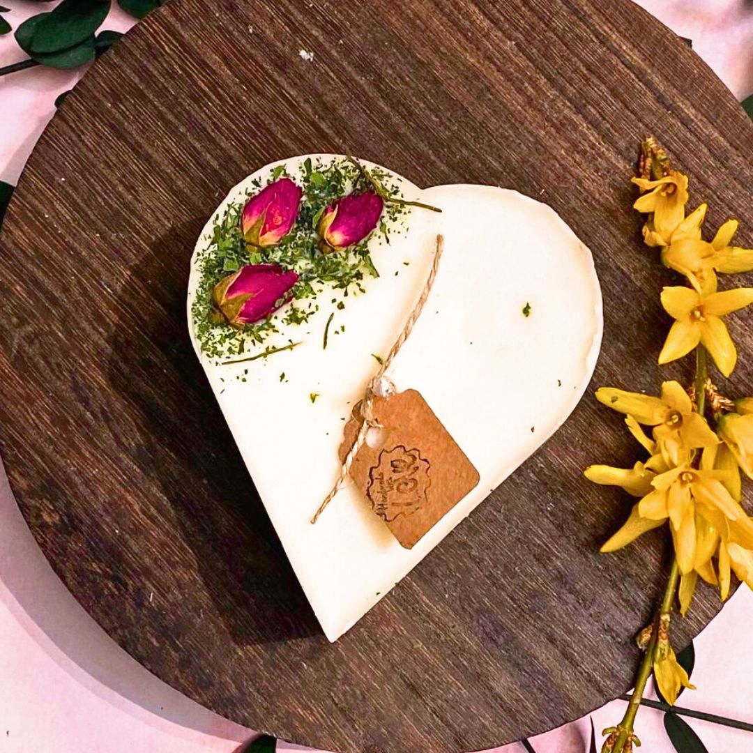 Heart-shaped white candle with pink flowers on a wooden board with yellow flowers.