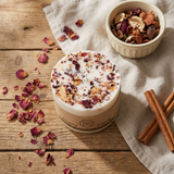 Small Beauty Scents rose petal candle on a rustic wooden table with scattered rose petals, cinnamon sticks, and potpourri, square image.