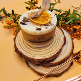 Small orange and cinnamon scented candle decorated with shredded cinnamon sticks on white soy wax background