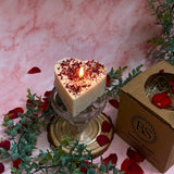 Burning Beauty Scents small heart rose petals candle with warm flame on crystal glass pedestal next to kraft gift box with pink marble background