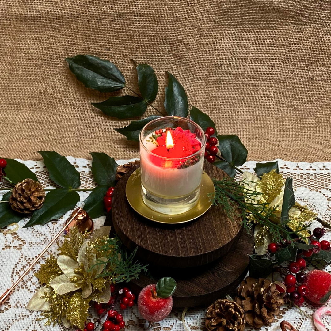 Small glass Winter Poinsettia candle top view with red poinsettia flower arrangement on white wax