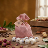 Pink drawstring bag with wax melts with lavender on a wooden surface with coffee beans and flowers.