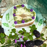 Heart-shaped candle with greenery and purple flowers on a decorative plate with blackberries and leaves.