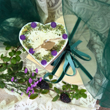 Heart-shaped gift box with purple flowers and green ribbon on a lace background