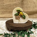 Heart-shaped candle with decorative elements on a wooden stand against a textured fabric background