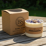 Candle with decorative elements and a cardboard box labeled 'Beauty Scents' on a wooden surface.