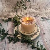 Large Wild Flowers soy candle 700g burning with lit flame and melted wax pool, blue cornflowers decoration visible, styled on ivy-patterned plate with fresh ivy and white lace - candle burning demonstration photography
