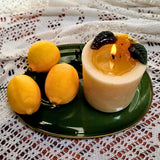 Burning medium lemon candle with wax pool and botanicals on green vintage plate with fresh lemons and lace
