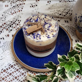 Medium Wild Flowers handmade soy candle 500g with blue cornflowers and dried botanicals, kraft gift tag, displayed on blue ceramic plate with white lace doily and variegated ivy leaves