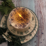 Medium Wild Flowers scented candle 500g burning with flame, dried blue cornflowers and botanicals on white soy wax, displayed on vintage ivy-patterned ceramic plate with rustic wooden background
