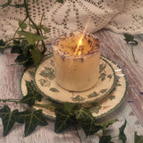 Medium Wild Flowers scented candle 500g burning with flame, dried blue cornflowers and botanicals on white soy wax, displayed on vintage ivy-patterned ceramic plate with rustic wooden background