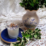 Small Glass Wild Flowers soy candle 400g in clear glass container with blue cornflowers decoration and  tag on blue ceramic plate, styled with white lace doilies, floral vase and fresh variegated foliage - glass container rustic lifestyle photography