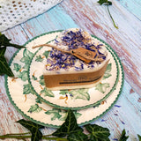 Small Heart Wild Flowers soy candle 300g with blue cornflowers decoration and Beauty Scents label on ivy-patterned plate, styled with fresh ivy leaves and white lace - heart-shaped rustic lifestyle photography