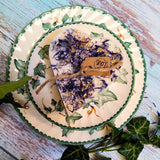 Small Heart Wild Flowers soy candle 300g with blue cornflowers decoration and Beauty Scents label on ivy-patterned plate, styled with fresh ivy leaves and white lace - heart-shaped rustic lifestyle photography