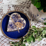 Small Heart Wild Flowers soy candle 300g with blue cornflowers decoration on blue ceramic plate, styled with white lace doilies and fresh variegated foliage - romantic heart-shaped lifestyle photography