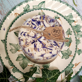 Small wild flowers candle with blue cornflowers and kraft LOVE tag on vintage floral china plate surrounded by fresh ivy leaves